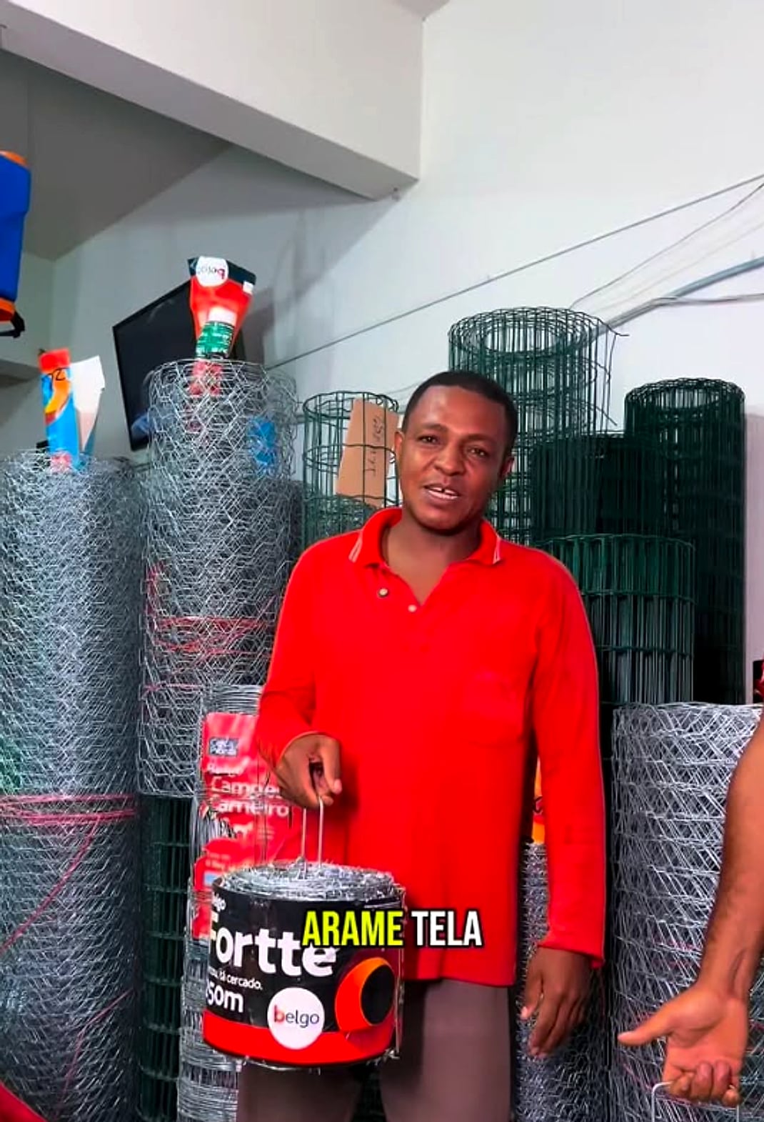 Funcionário segurando rolo de arame farpado Motto Belgo entre rolos de tela