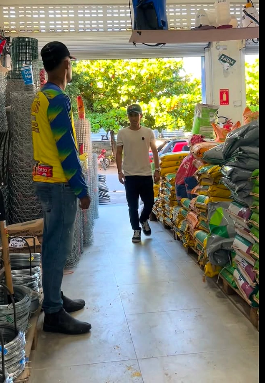 Corredor da loja com rolos de tela e arame de um lado e sacos de ração do outro